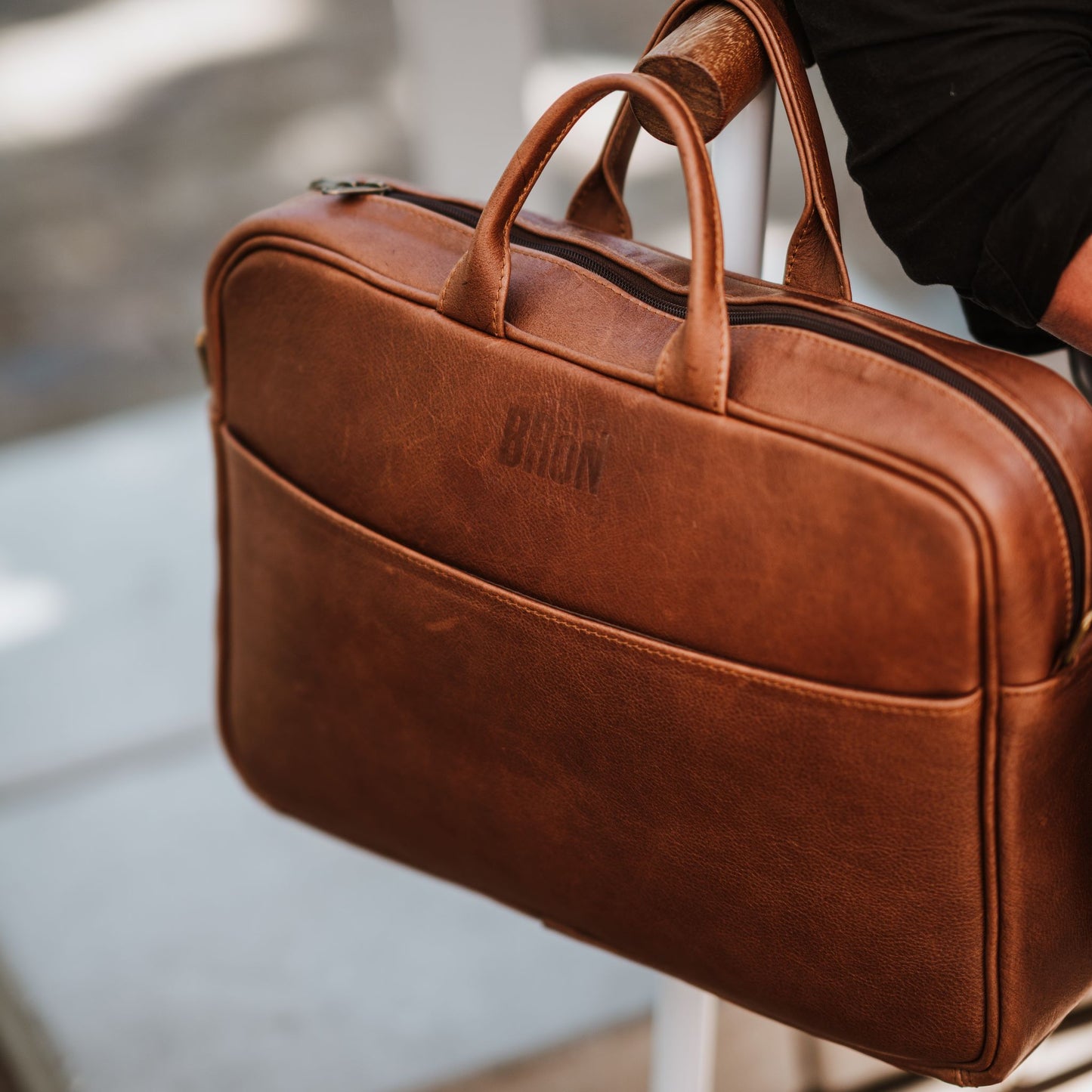 Front view of leather laptop bag, showcasing front sleeve pocket, handles and top zipper.