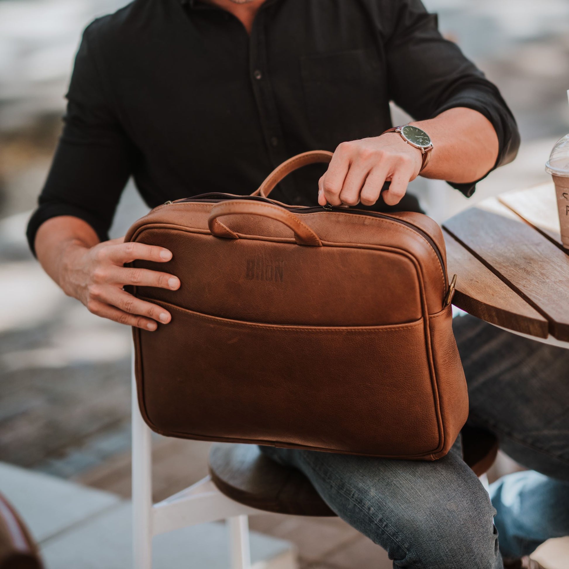 Front view of leather laptop bag, showcasing front sleeve pocket, handles and top zipper.