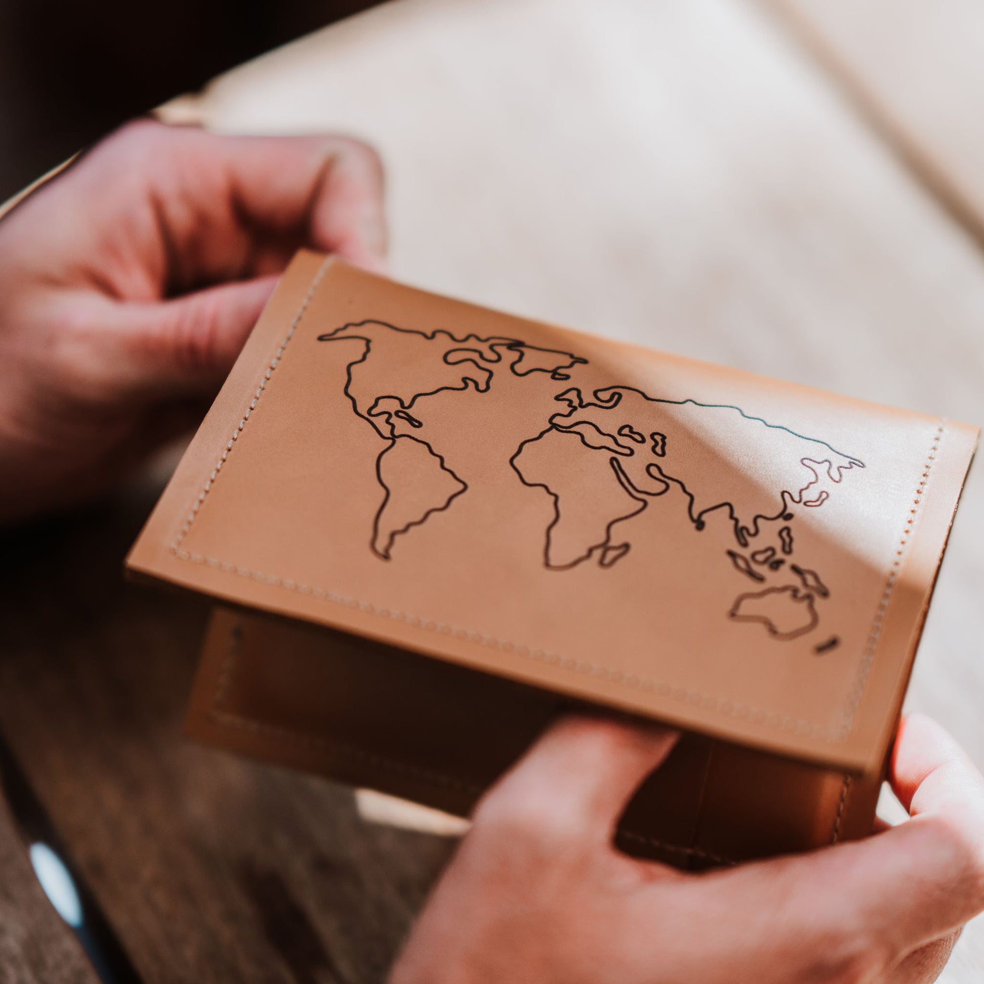 Front view (with engraved world map) of leather passport holder and travel wallet.