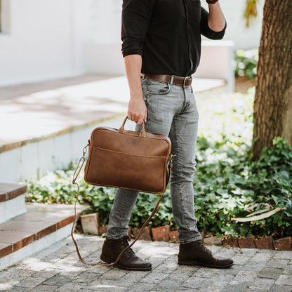 Front view of leather laptop bag, showcasing front sleeve pocket, handles and shoulder strap.