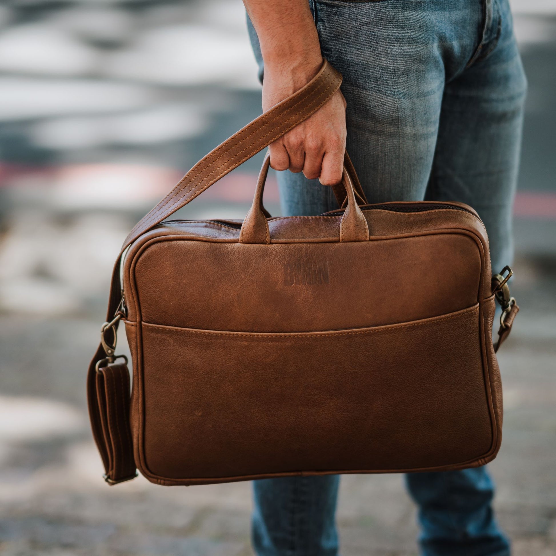 Front view of leather laptop bag, showcasing front sleeve pocket, handles and shoulder strap.