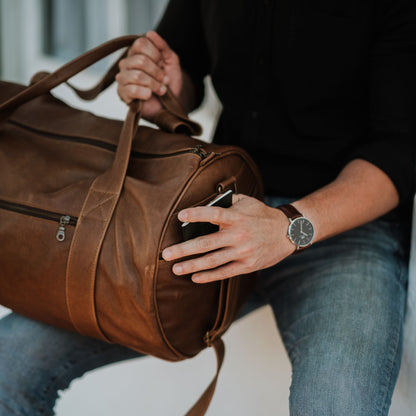 Side view of leather duffel bag, showcasing the handles, shoulder strap and side sleeve pocket.