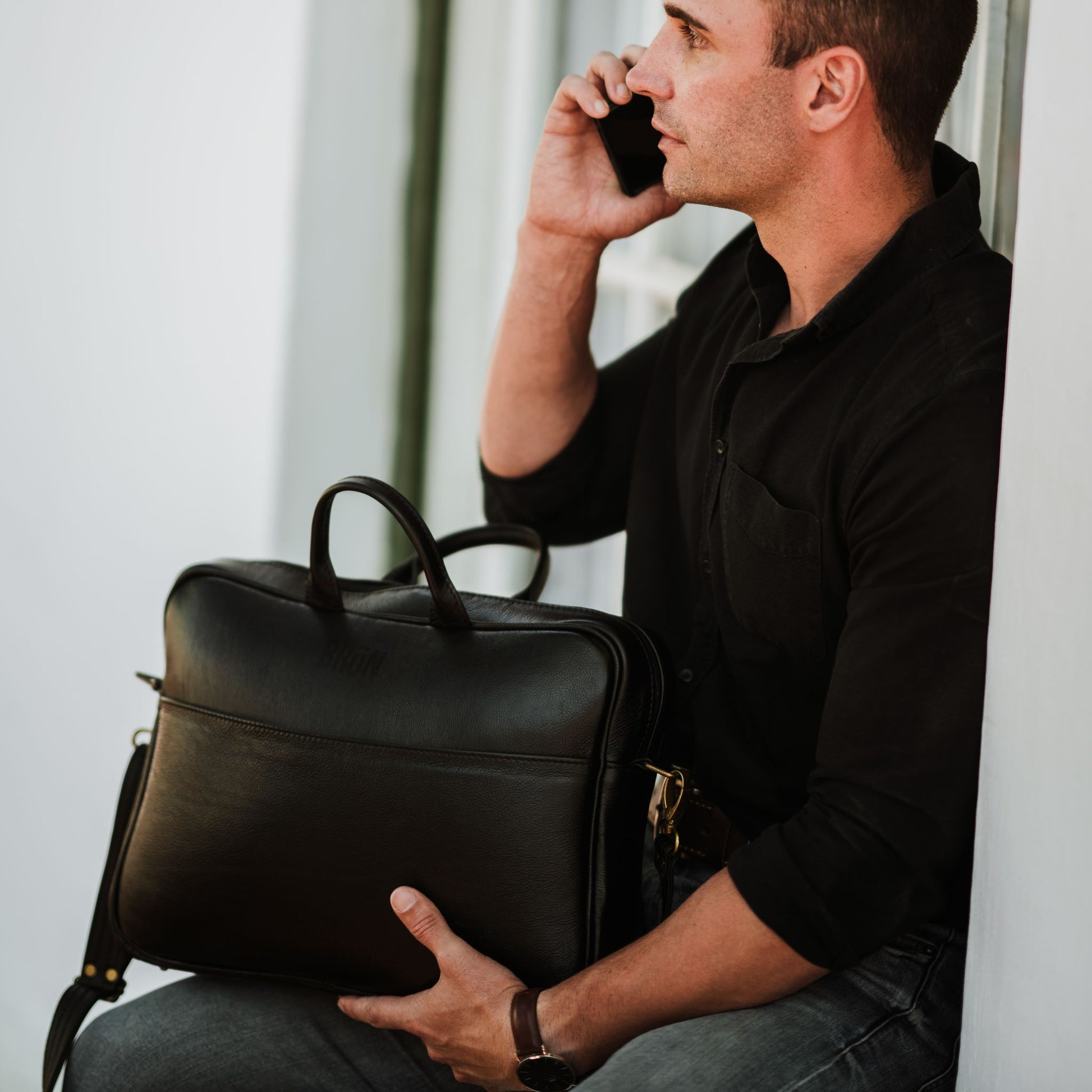 Front view of leather laptop bag, showcasing front sleeve pocket and handles.