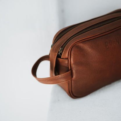 Front and side view of the leather toiletry bag, showcasing the handle and top zipper.