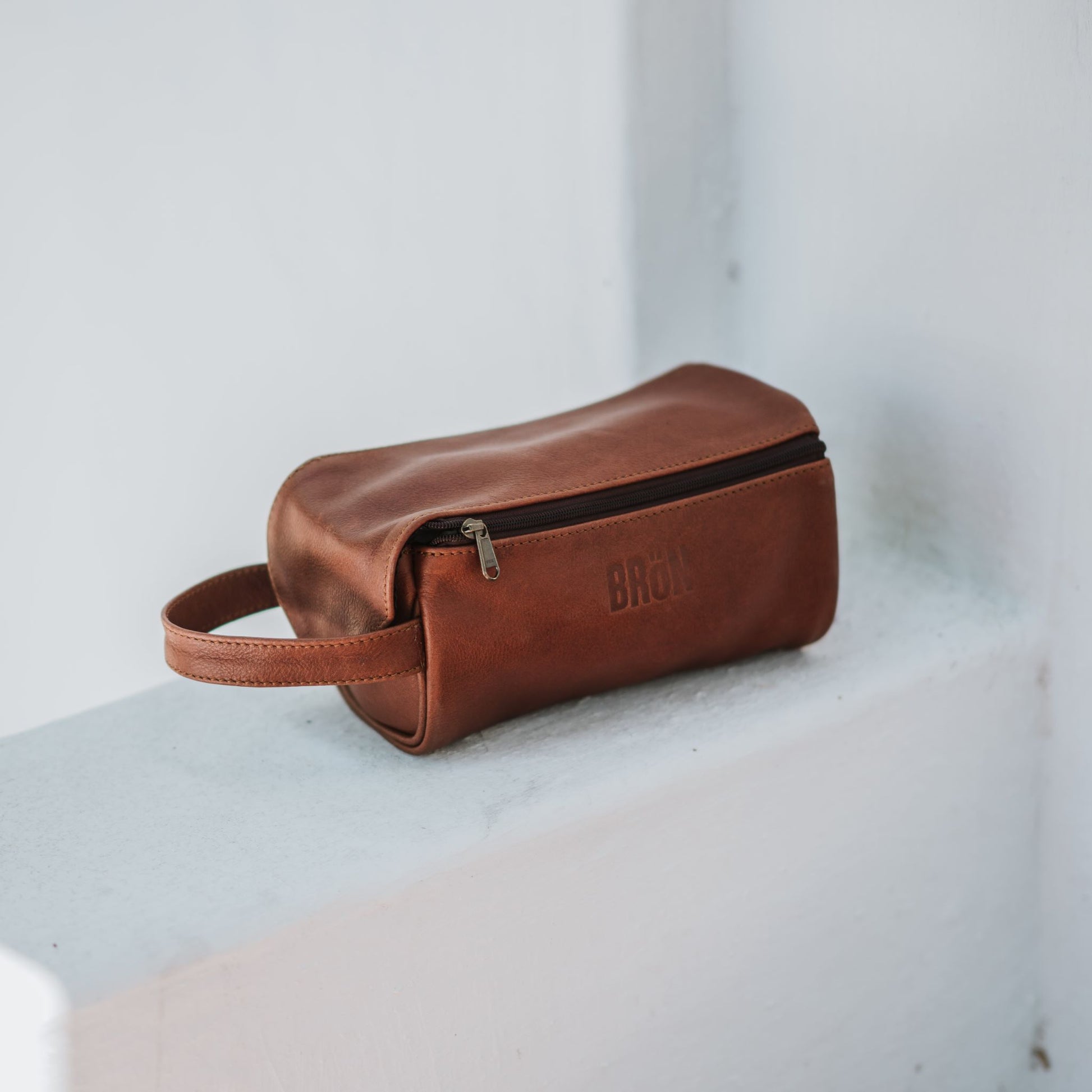 Front and side view of the leather toiletry bag, showcasing the handle and top zipper.