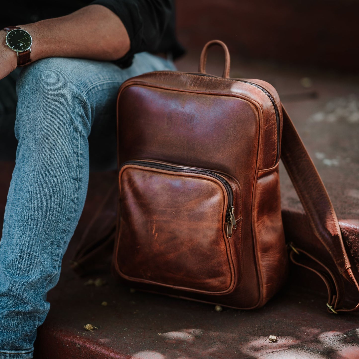 Front view of the leather laptop backpack, showcasing the front zip pocket, shoulder straps and handle.