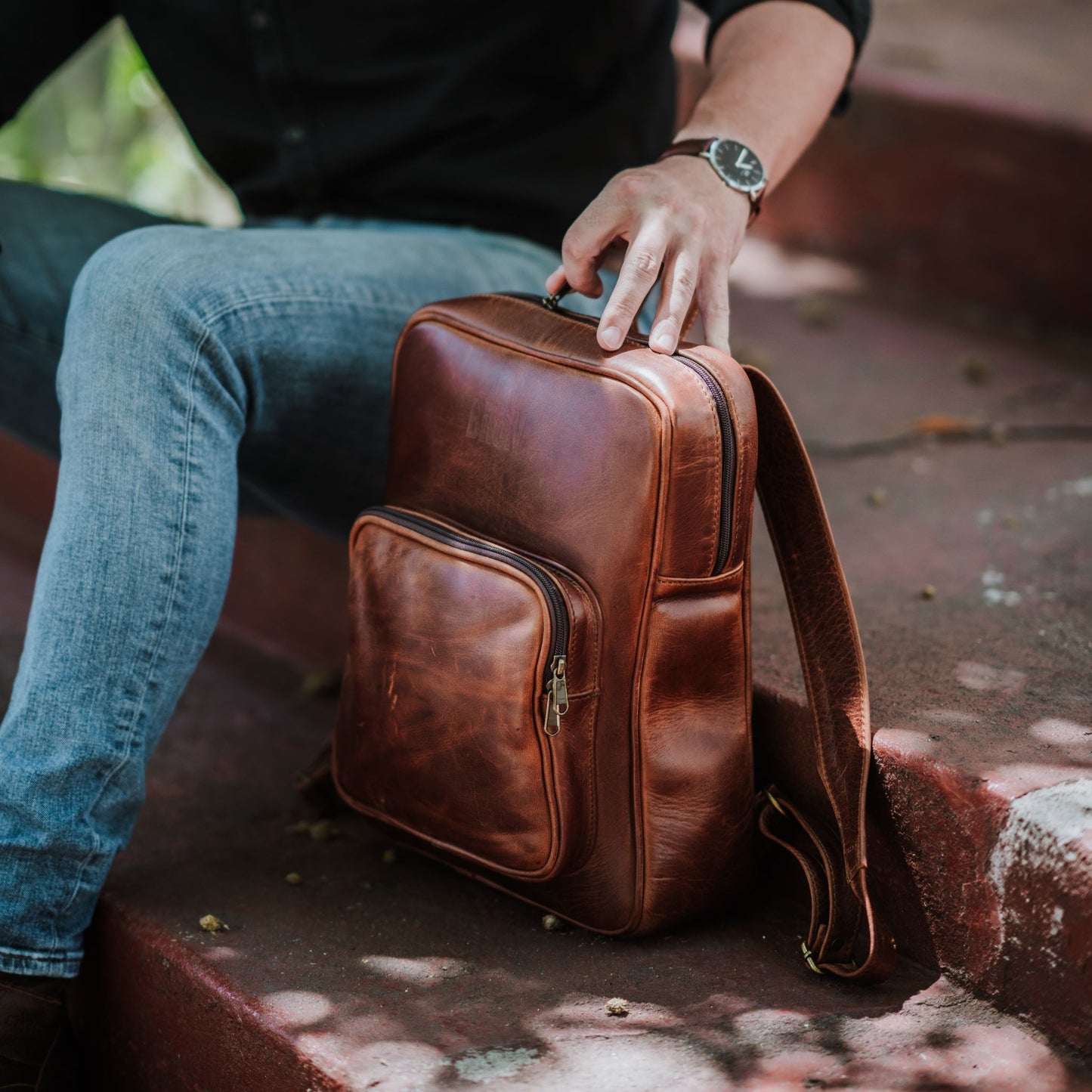 Front and side view of the leather laptop backpack, showcasing the front zip pocket, top zipper, shoulder straps and handle.