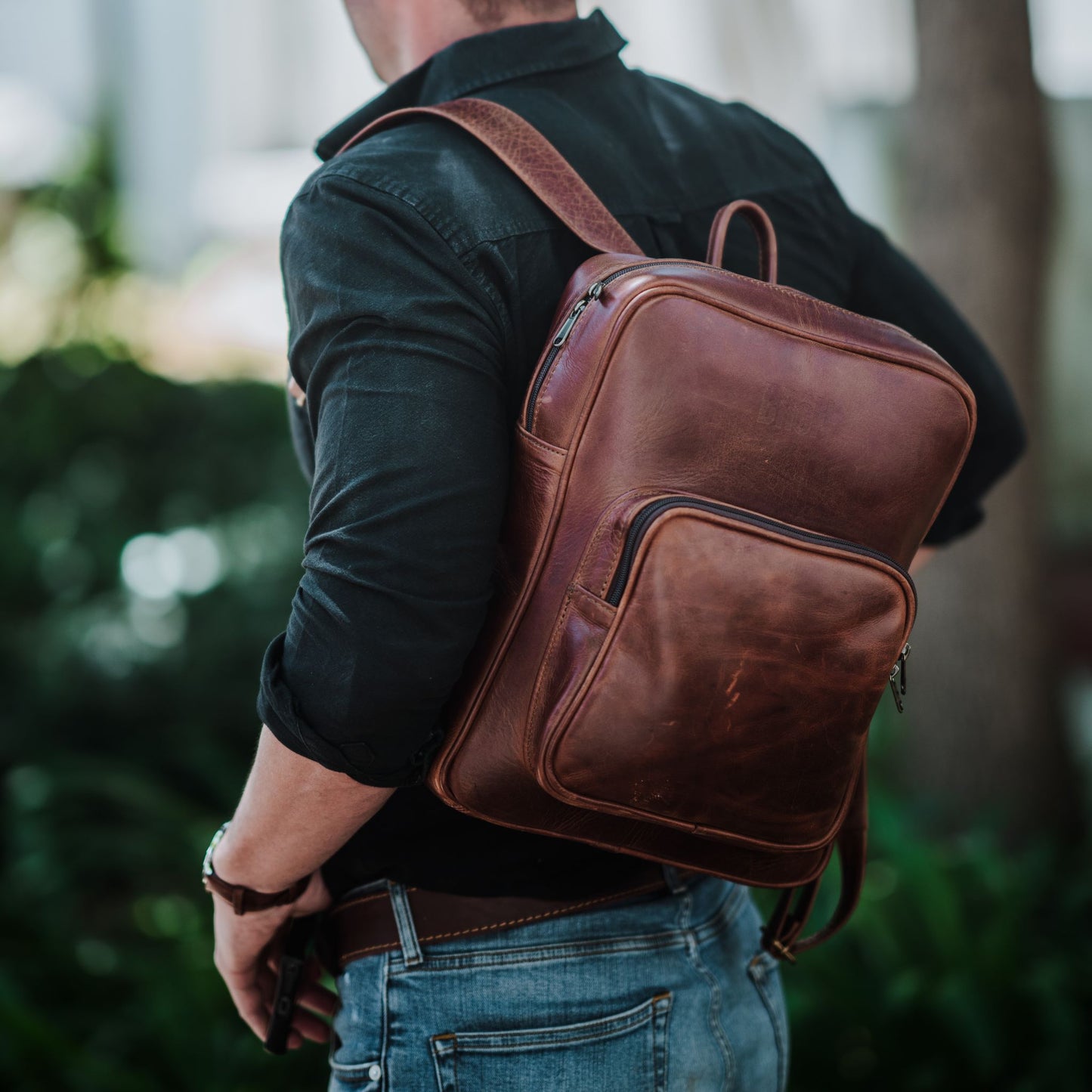 Front view of the leather laptop backpack, showcasing the front zip pocket, shoulder straps and handle.