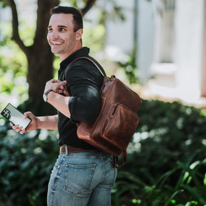 Front and side view of the leather laptop backpack, showcasing the front zip pocket, top zipper, shoulder straps and handle.