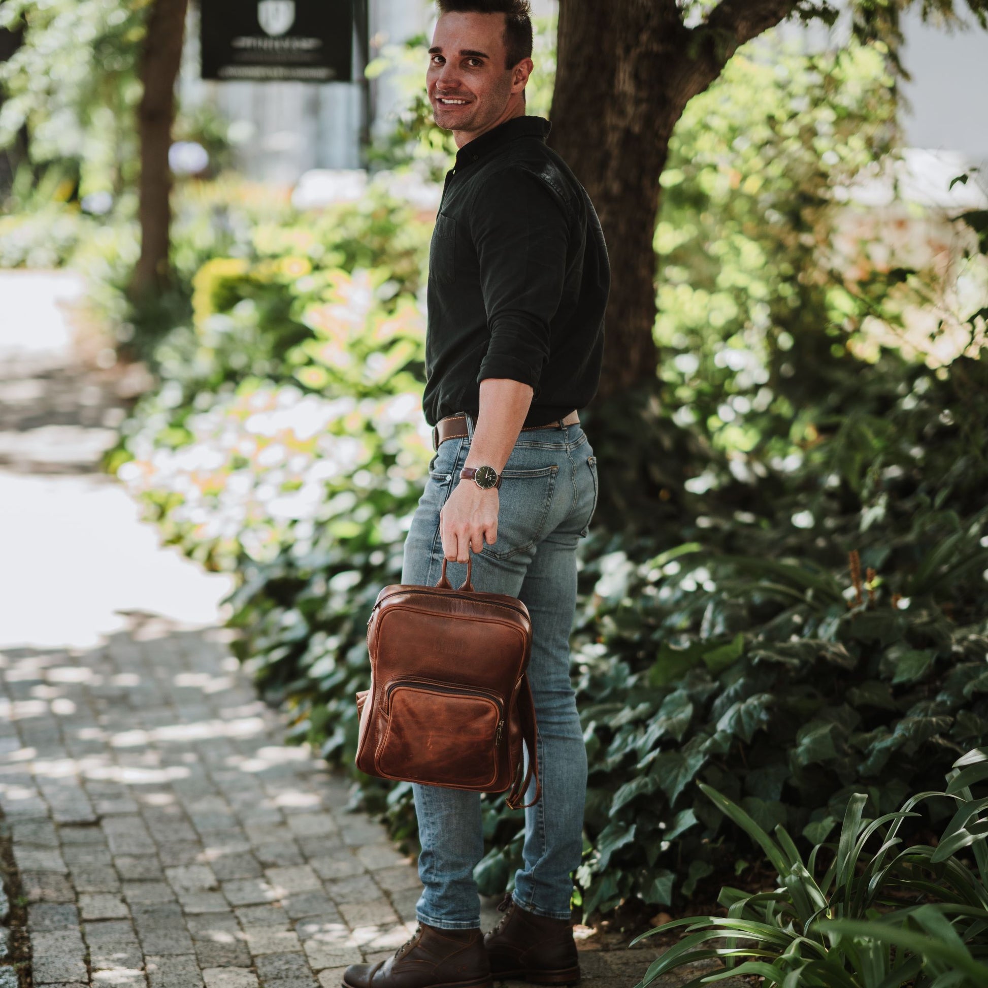 Front view of the leather laptop backpack, showcasing the front zip pocket, shoulder straps and handle.