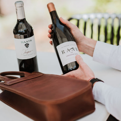 Front and side view of the leather wine carrier, showcasing the handles and two bottles of wine.