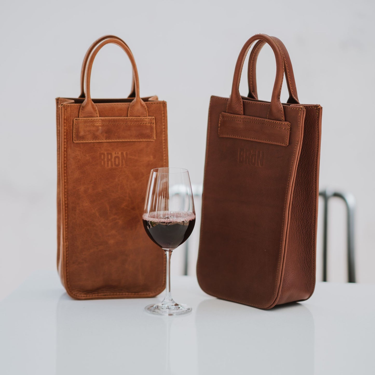 Front view of two leather wine carriers, showcasing the handles and a glass of wine.