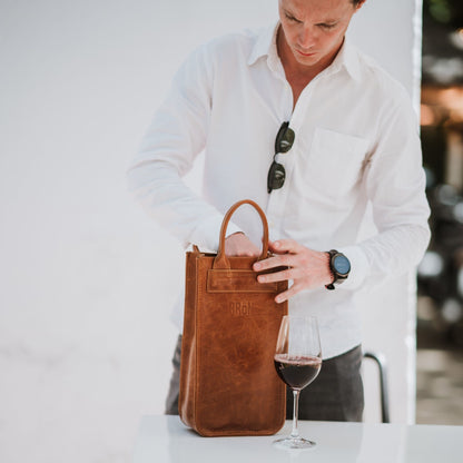 Front view of the leather wine carrier, showcasing the handles and a glass of wine.