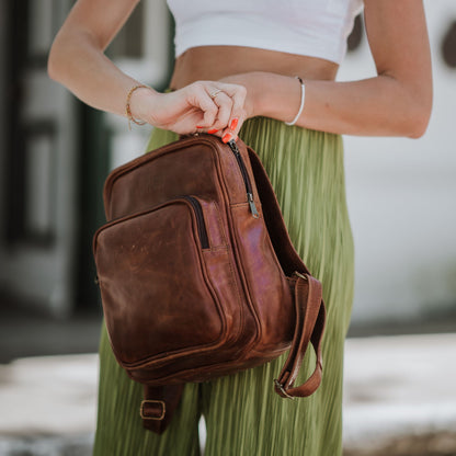 Front and side view of the small leather backpack, showcasing the front zip pocket, shoulder straps and handle.